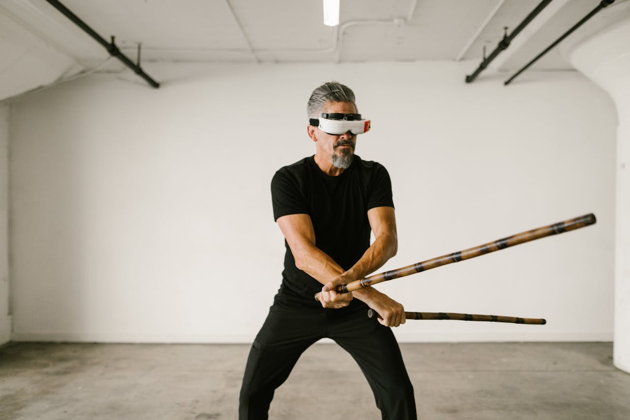 Man practicing martial arts with virtual reality headset and arnis sticks indoors.